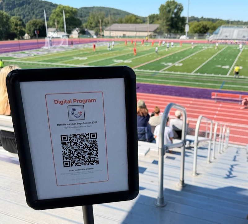 A printed QR code invite for a digital program on display at a high school soccer game